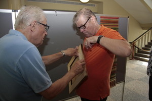 Jorma Kujala apujoukkoineen asettaa omia maalauksiaan n&auml;yttelysermeihin.