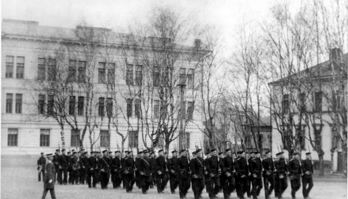 Kuva Haminan kadettikoulun uudesta päärakennuksesta, nykyinen RUK:n päärakennus, ja sen vieressä ”Kanakopista” ajoittuu vuosiin 1898–1903. Marssiharjoituskuva on Haminan kaupunginmuseon kokoelmista.